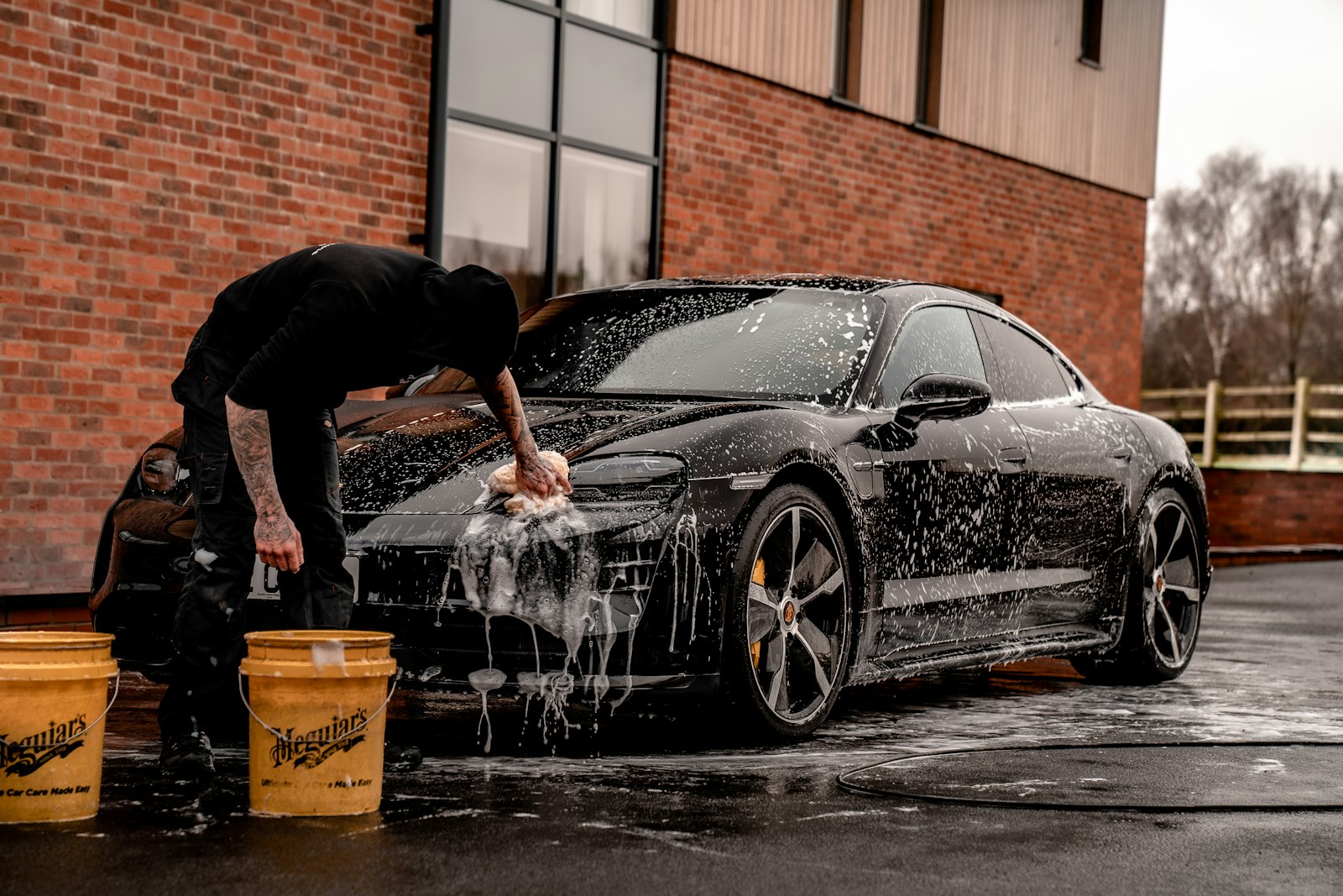 Detailer hand washing a vehicle on location with foam and dual buckets